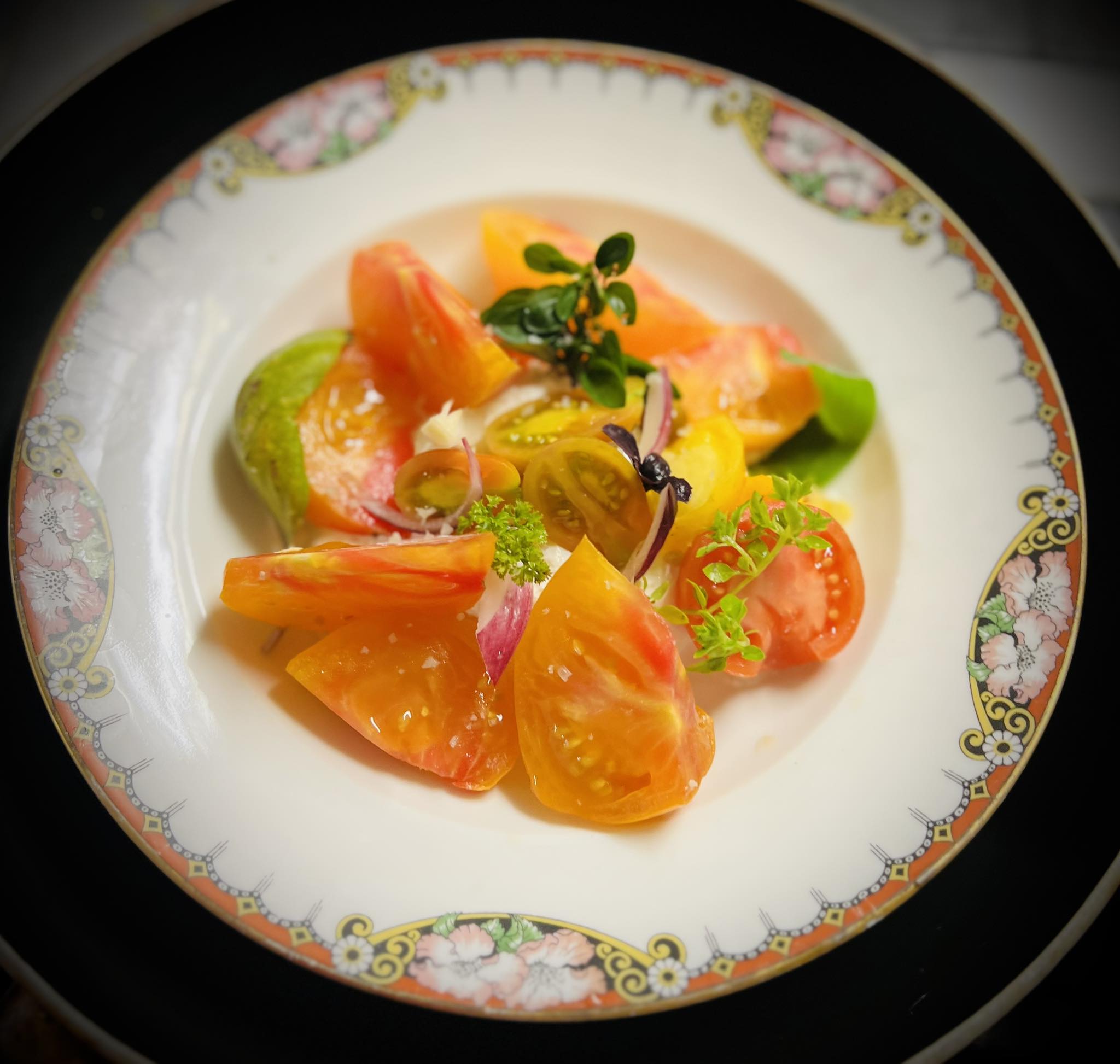 Assiette de tomates colorées variées : rouge, jaune, verte, avec herbes fraîches